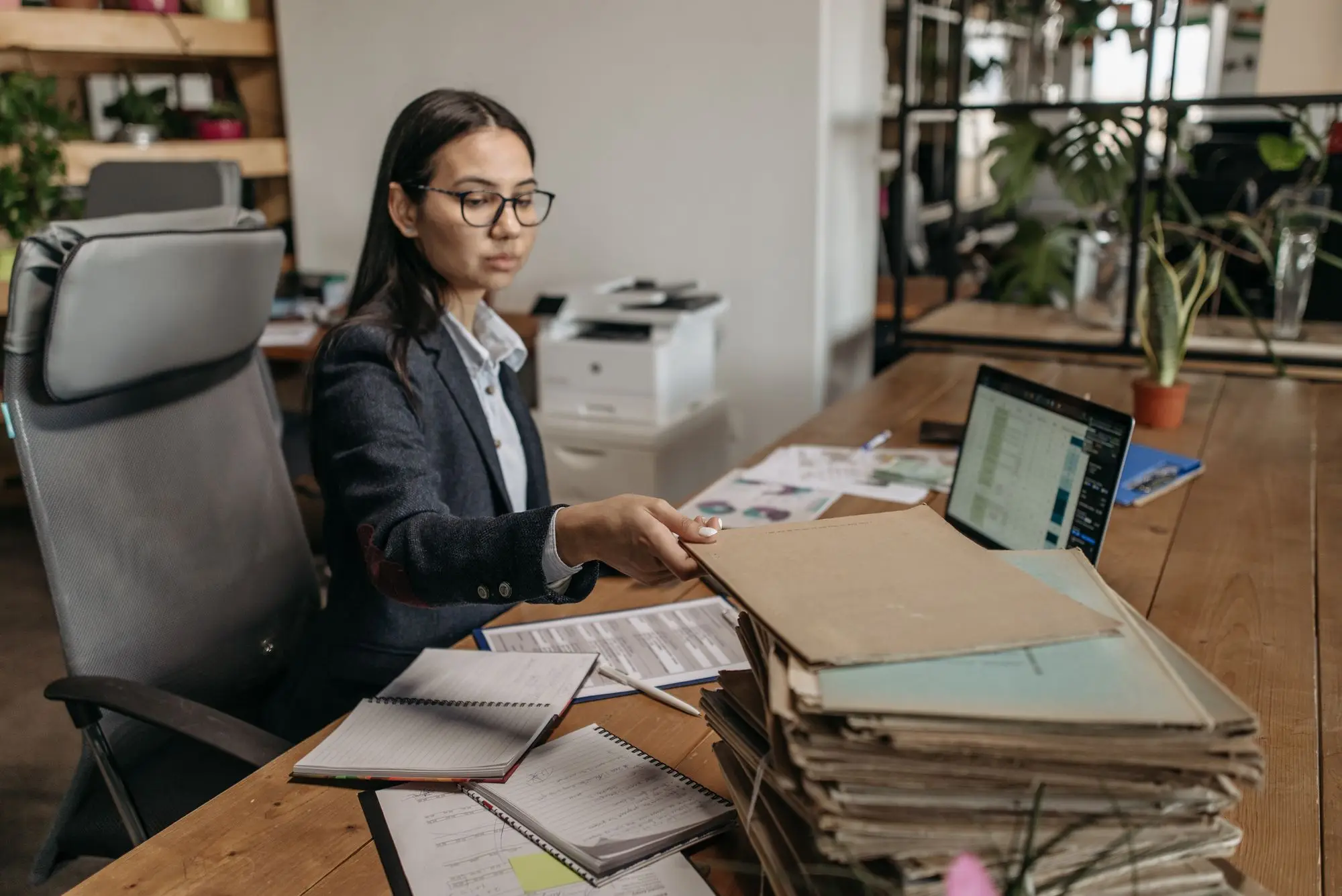 Credit assessor at a wooden office desk working through a stack of application files beside a laptop