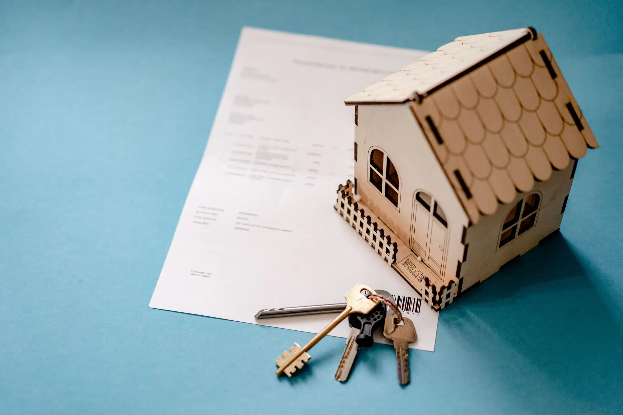 Home loan contract on a desk beside a small wooden model house and a set of house keys, ready to be signed